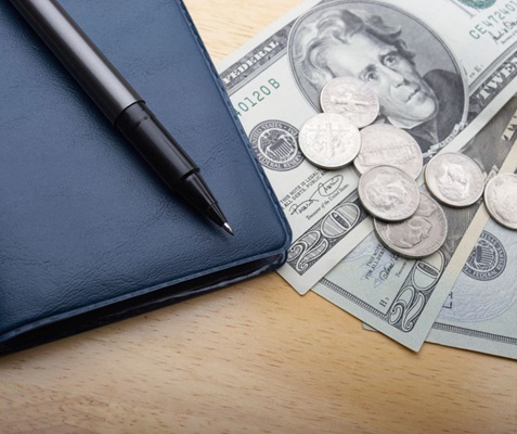 Checkbook open A checkbook sits next to three twenty dollar bills and some change.